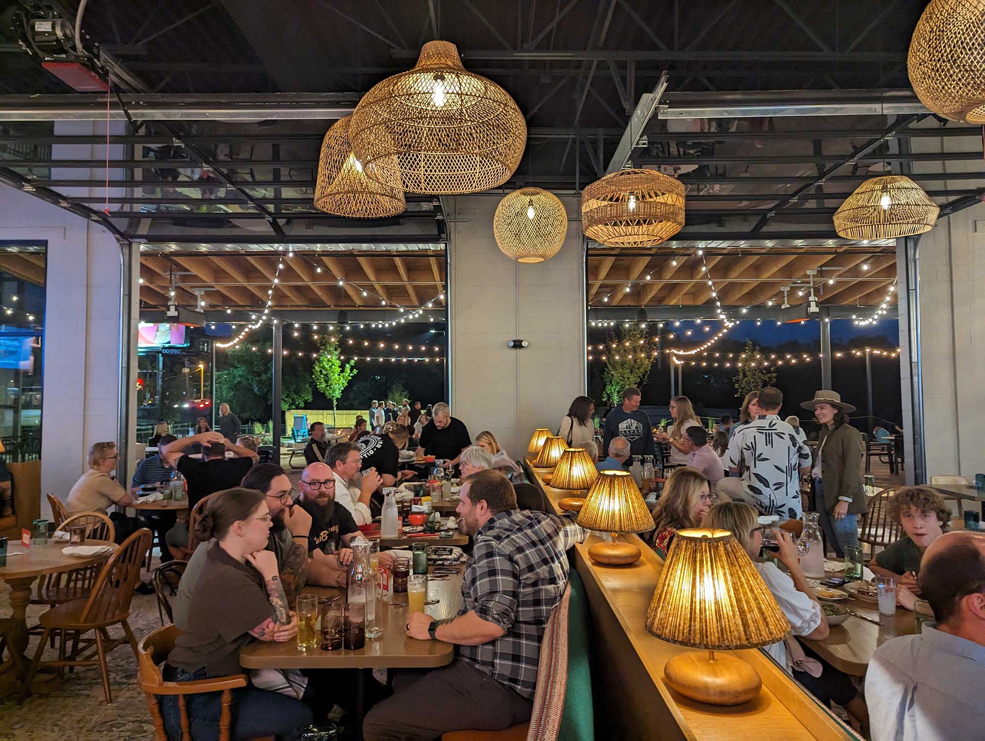 Interior of Either Or at night with people seated at tables facing open garage doors to the patio